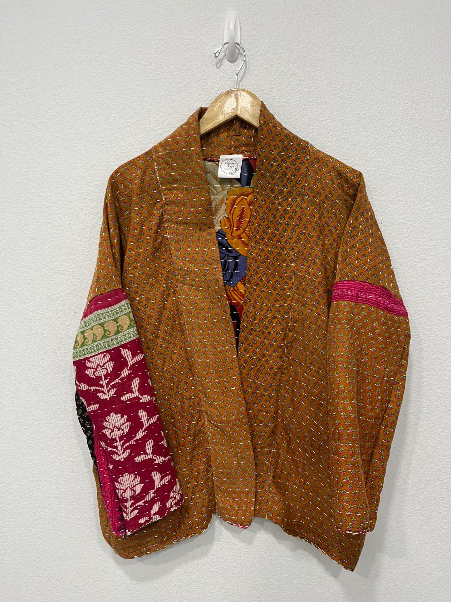 This one-of-a-kind quilted brown-gold small floral print and pink upper arm bands jacket is made of Kantha Cloth. It is wonderful for traveling as it is reversible for 2 looks in one and it is light weight for easy packing.